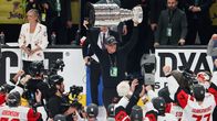Jääkiekkojoukkue juhlii jäällä Stanley Cup -pokaalin kanssa, taustalla näkyy mediaväkeä ja mainostauluja.