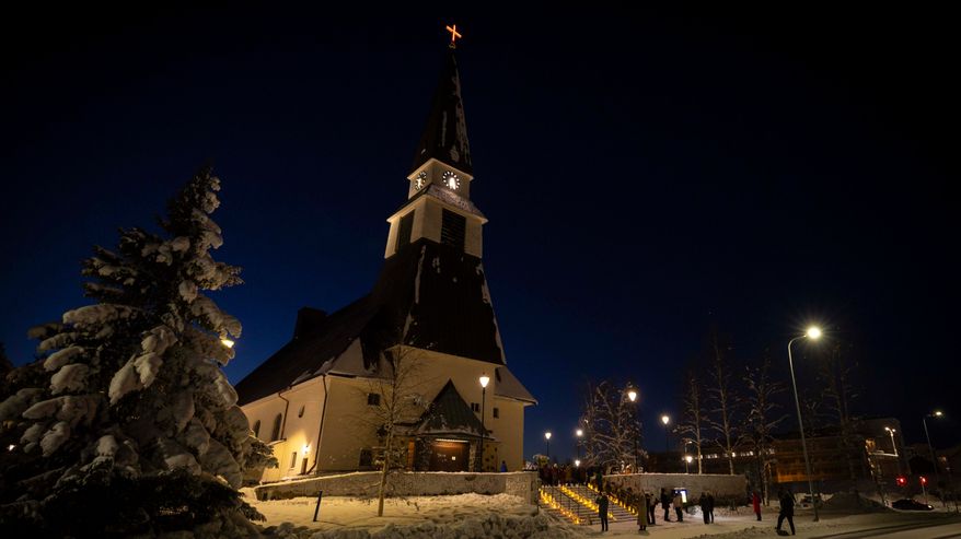 Rovaniemen kirkko lumisessa maisemassa, portailla on kynttilöitä.
