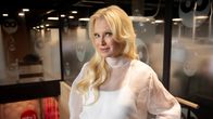 Linda Lampenius iklädd en helvit byxdress står och ser rakt in i kameran och ler.