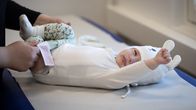 Vauva makaa hoitopöydällä päiväunien jälkeen ja venyttelee, samalla kun häntä riisutaan.