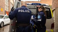Poliisit saattavat henkilöä rakennuksesta poliisiautoon.