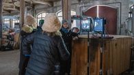 Några personer står i en gammal fabrikshall och följer med en filminspelning via två olika skärmar.