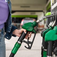Close up photo of a woman in denim jacket and jeans by a petrol pump, taking the fuel nozzle from the unit.