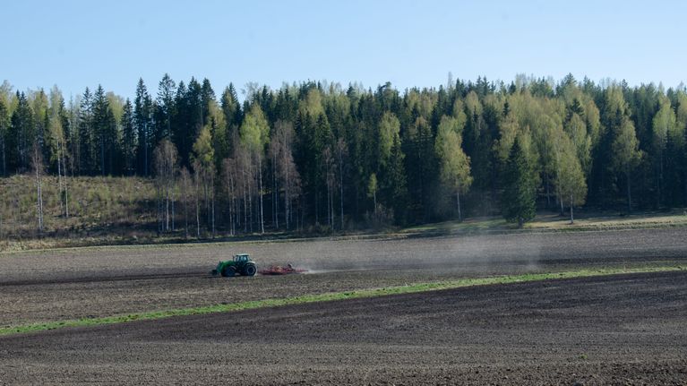 Traktori kyntää laajalla peltoaukeamalla.