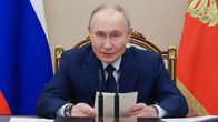 Vladimir Putin istuu mikrofonien edessä pitäen papereita käsissään.