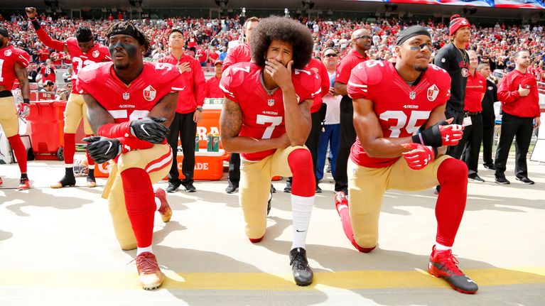 Colin Kaepernick ja kaksi muuta pelaajaa polvistuneena.