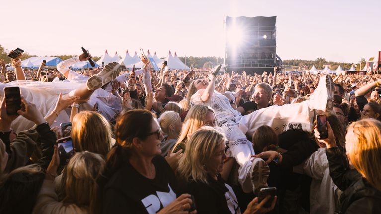 Paula Vesala ja Mira Luoti heittäytyvät yleisön päälle Ruisrockissa PMMP:n keikalla. Taustalla valospotti ja yleisöä. 