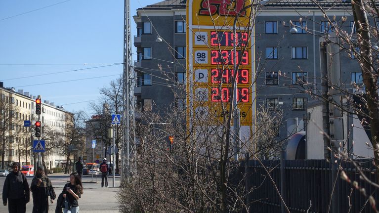 Katunäkymässä ihmisiä ja huoltoaseman kyltti, jossa 95-bensiinin hinta on yli kaksi euroa.