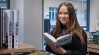 Pitkähiuksinen nainen kirjakaupassa selaa kirjaa, jonka kannessa lukee otsikko "Hildur". 