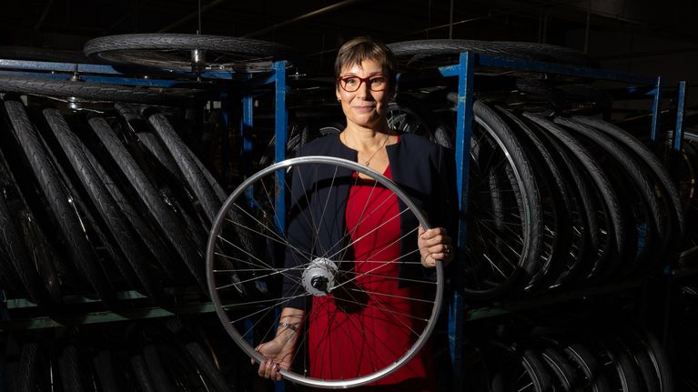 Henkilö seisoo varastossa, jossa on polkupyöränrenkaita ja pitää pyörän vannetta käsissään. 