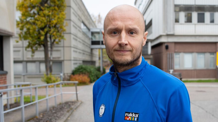 Närilb på en man i blå träningsjacka. I bakgrunden syns betongbyggnader.