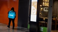 Photo shows a Wolt courier walking past a restaurant.