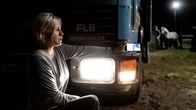 Nainen kuvaa salaa puhelimella auton takaa.