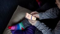 Person seen from above sitting cross-legged on a sofa, holding and using a smartphone with both hands.