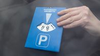 Lähikuva autonkuljettajan kädestä, joka laittaa pysäköintikiekon kojelaudalle.