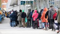 Seinän vierustaa pitkin menevä pitkä jono lämpimästi pukeutuneita ihmisiä. 
