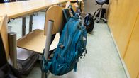 An empty classroom with a backpack hanging from a chair in focus. 