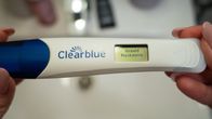 Close up photo of a woman's hands holding a white and blue plastic home pregnancy test, with a screen that reads 'pregnant' in Finnish and Swedish.