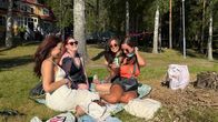Naisporukka istuu viltillä nurmikolla. Kaikki hymyilevät.