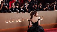 Nainen mustassa iltapuvussa seisoo kameraryhmän edessä kultaisella taustalla, jossa lukee GOLDEN GLOBES.