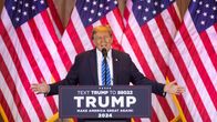 Donald Trump puhuu mikrofoniin kädet levellään puhujankorokeelta lavalta. Taustalla Yhdysvaltain lippuja.