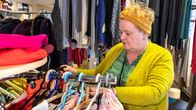 Asiakaspalveluohjaaja järjestelee vaatteita kirpputorilla.