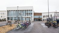 Rakennuskuva modernista vaaleasta koulusta, jonka pihalla on pyöriä parkissa.