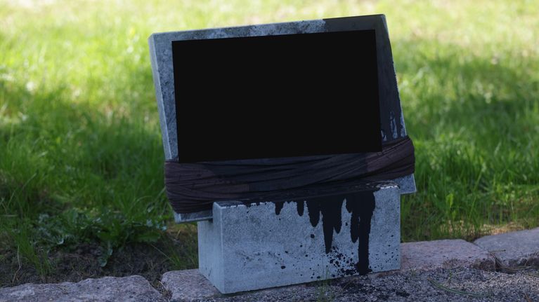 Kuvassa mustalla nesteellä vandalisoitu hautakivi. Kuvaa on muokattu siten, että kuvasta on peitetty hautakiveen kaiverrettu nimi.