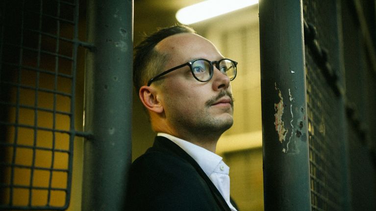 Henkilö seisoo rautaportin edessä hämyisessä valaistuksessa.