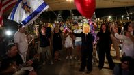 Ihmiset juhlivat kadulla. Yhdellä ihmisellä on Trump-naamio. Ilmassa on Israelin ja Yhdysvaltain liput.