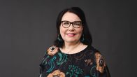 A dark-haired smiling woman with glasses, Merja Ylä-Anttila, looks smiling in to the camera.