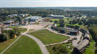 Flygfoto av ett område med blandad bebyggelse, inklusive en idrottsanläggning med fotbollsplan, skolbyggnader, och bostadshus. 