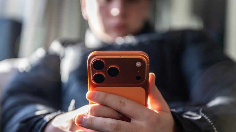 A young person holding an iPhone 17 mobile phone in their hands.