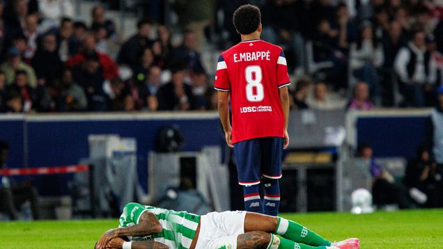 Ethan Mbappe seisoo jalkapallokentällä selin vastustajaansa joka makaa maassa kasvojaan pidellen.