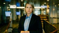 Nainen seisoo isätilassa pukeutuneena siniseen raidalliseen paitaan ja mustaan bleiseriin. 