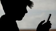 A boy scrolls through his phone in a silhouetted image. 