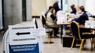 Människor sitter i en vallokal. I förgrunden syns en bild där det står "förhandsröstning"
