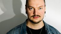 Henkilö seisoo valkoisen seinän edessä, ja valo heijastaa hänen varjonsa taustalle.