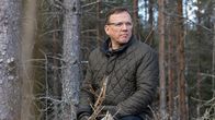 Erkki Kerola istuu metsässä kiven päällä.