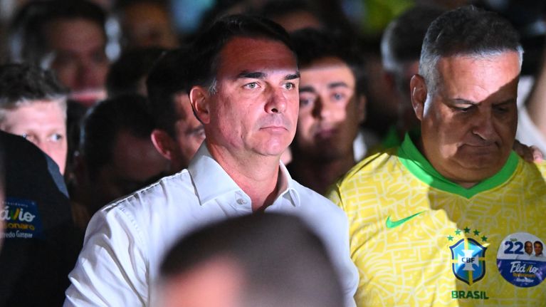 En man i vit skjorta står bredvid en man i gul Brasilien-tröja. Flera personer syns i bakgrunden.