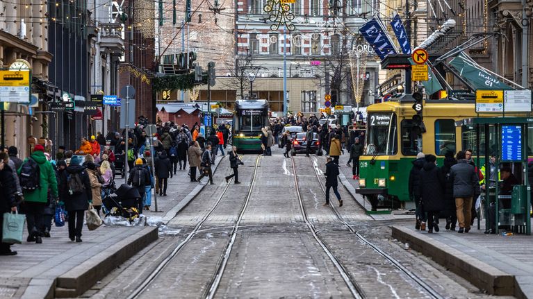 Vilkas katunäkymä Helsingin keskustasta joulun aikaan, ihmisiä kävelemässä ja raitiovaunut kulkemassa Aleksanterinkadulla.