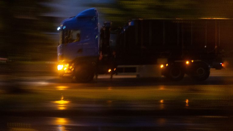 Kuorma-auto kiitää öisellä, märällä tiellä.