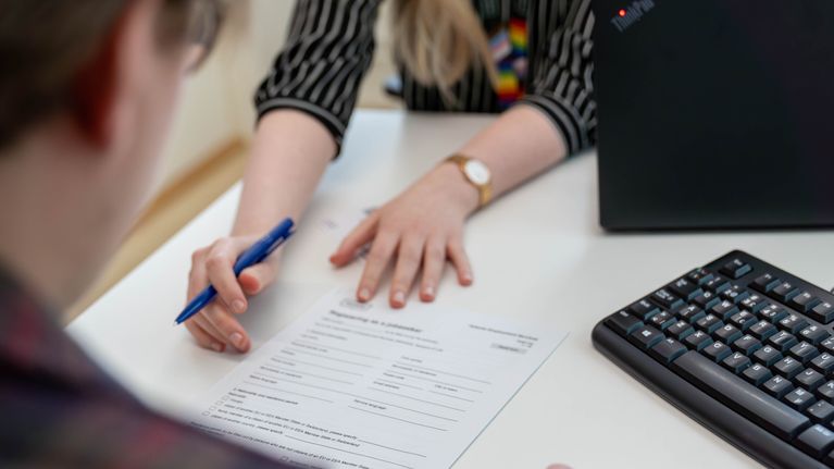 Photo shows a form on a desk and two people looking at it.