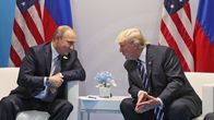 Putin katsoo hymyillen Trumpia, istuvat miehet ovat kumartuneet juttelemaan, liput taustalla.  