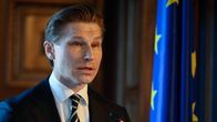 A man in a suit and tie, Antti Häkkänen, speaking next to an EU flag.