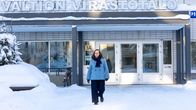 Nainen kävelee vaaleista tiilistä rakennetun virastotalon edustalla aurinkoisena talvipäivänä.