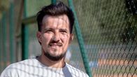 Mustatukkainen mies seisoo tenniskentällä verkon vieressä.