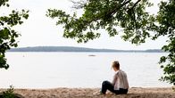 Henkilö istuu rannalla ja riisuu lenkkareita pois jalasta.