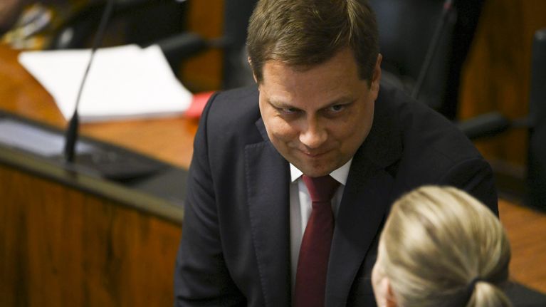 Vilhelm Junnila katsoo etualalla olevaa henkilöä eduskunnan istuntosalissa.