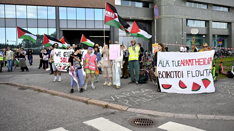 About 15 people hold Palestinian flags and banners on a city sidewalk. 